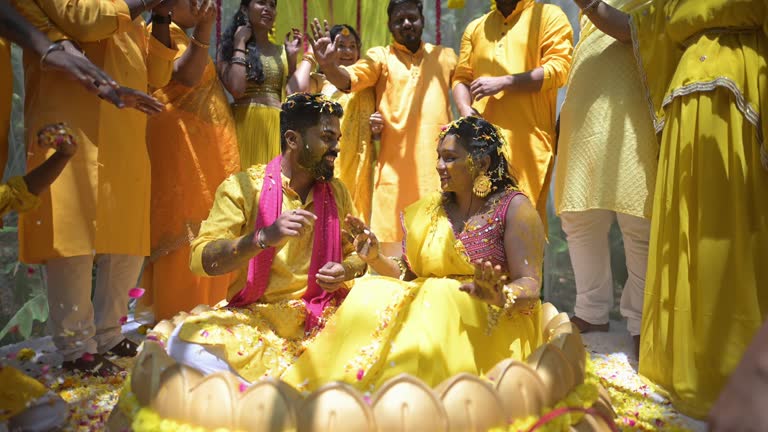 Festive wedding celebration with bride and groom in colorful attire surrounded by guests dancing and vibrant floral decorations